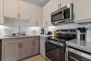 A modern kitchen with light wood cabinets, stainless steel appliances, and a granite countertop. - Stylish 1 King BR suite-Domain Gym, Pool & Parking (Austin)