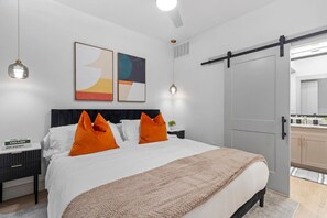 Een moderne slaapkamer met een bed, twee kussens, een nachtkastje, een wandlamp en een schuifdeur naar een badkamer.