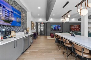 A modern kitchen with a bar area, a coffee station, and a dining space with bar stools. - Stylish 1 King BR suite-Domain Gym, Pool & Parking (Austin)