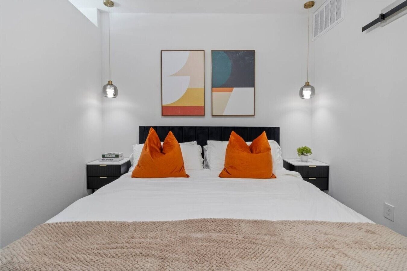 A modern hotel room with a large bed, two nightstands, a small plant, and abstract artwork on the wall.