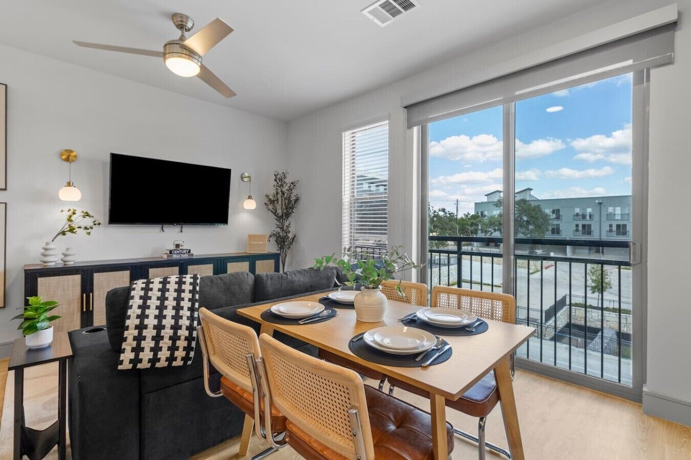 A modern dining area with a table set for four, a sofa, and a television on the wall.