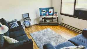 Ein Wohnzimmer mit Flachbildfernseher, Couch, Teppich und Couchtisch.