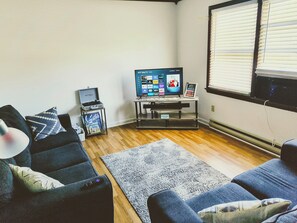 A living room with a flat-screen TV, a coffee table, a sofa, and a rug.