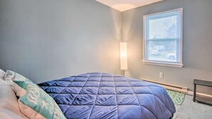 Ein Schlafzimmer mit einem Bett, einem Nachttisch, einer Lampe, einem Fenster mit Jalousien und einem Teppichboden.