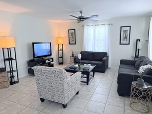 A modern living room with a flat-screen TV, a sofa, a coffee table, and a patterned armchair. - 3-bedroom bungalow in peaceful George Town with AC (George Town)