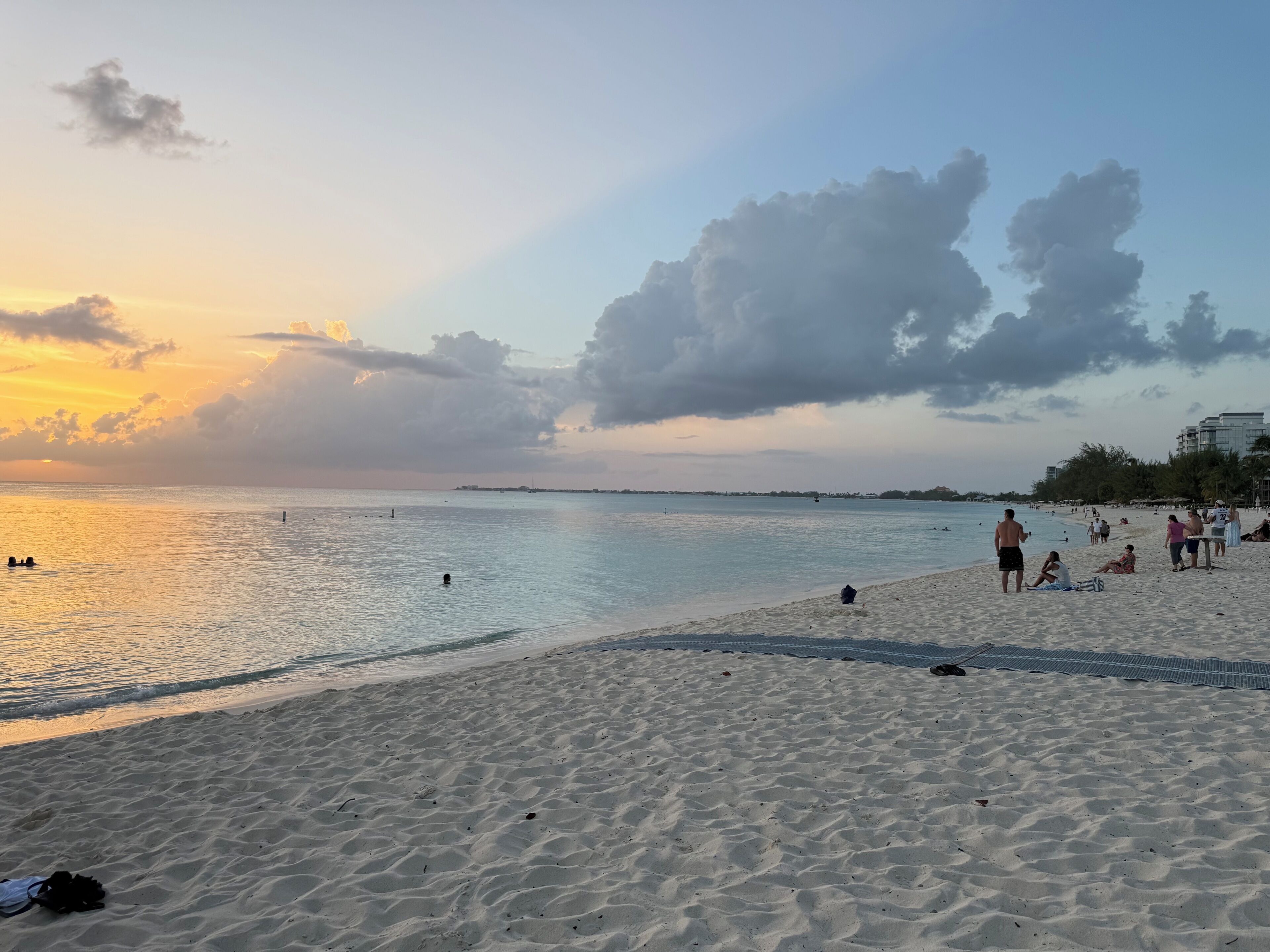 A beach with people, a calm sea, and a sunset.