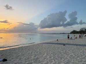 A beach with people, a calm sea, and a sunset.
