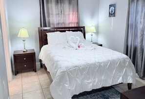 A neatly made bed with a white duvet and pillows, two bedside lamps, a wooden nightstand, and a framed picture on the wall. - 2-bedroom bungalow in peaceful George Town with AC (George Town)