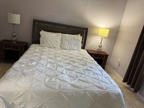 A neatly made bed with a quilted cover, two bedside tables with lamps, and a plain wall with a light switch. - 3-bedroom bungalow in peaceful George Town with AC (George Town)