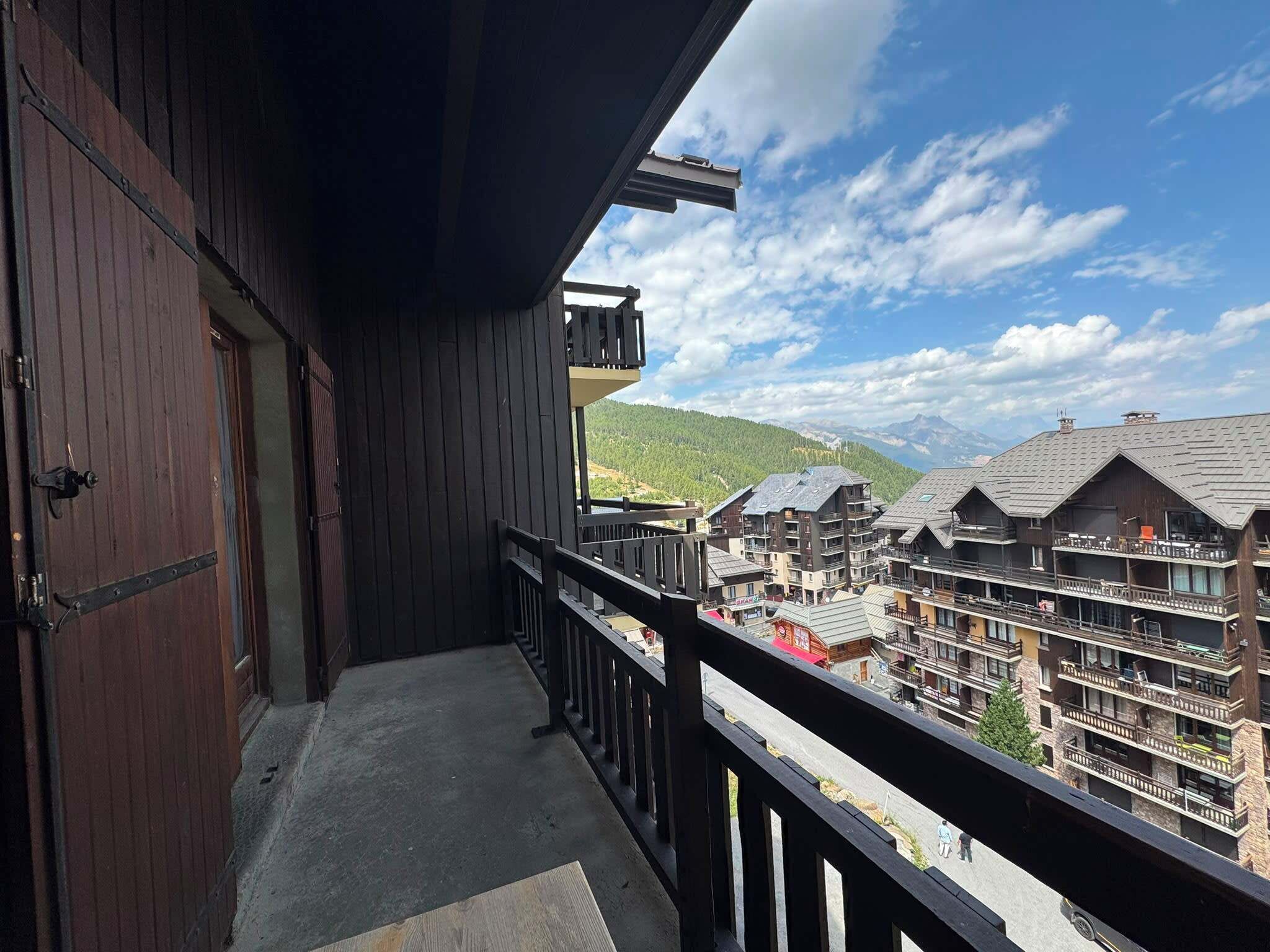 Ein Holzhaus mit Balkon mit Blick auf eine gebirgige Gegend mit mehreren Gebäuden.