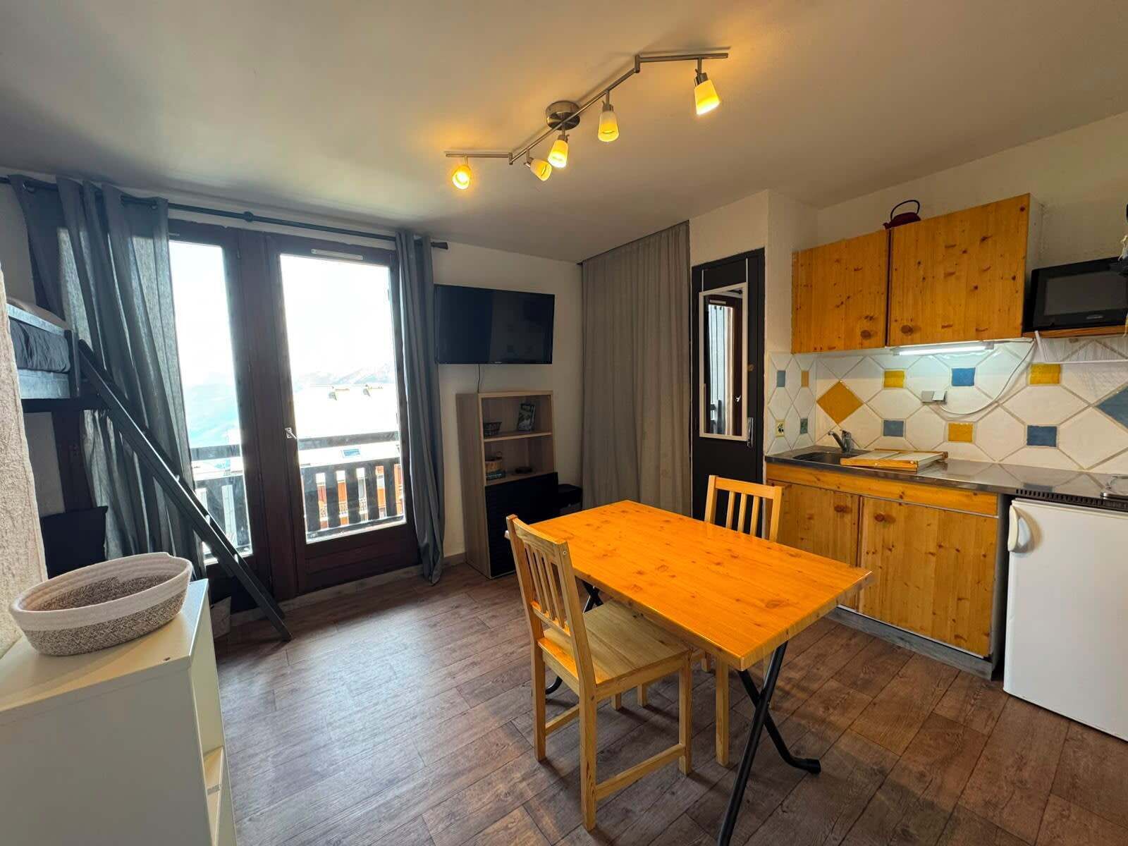 Een compacte keuken met houten kastjes, een eettafel en een inbouwoven.