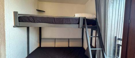 A bunk bed with a ladder, a window with curtains, and a door.