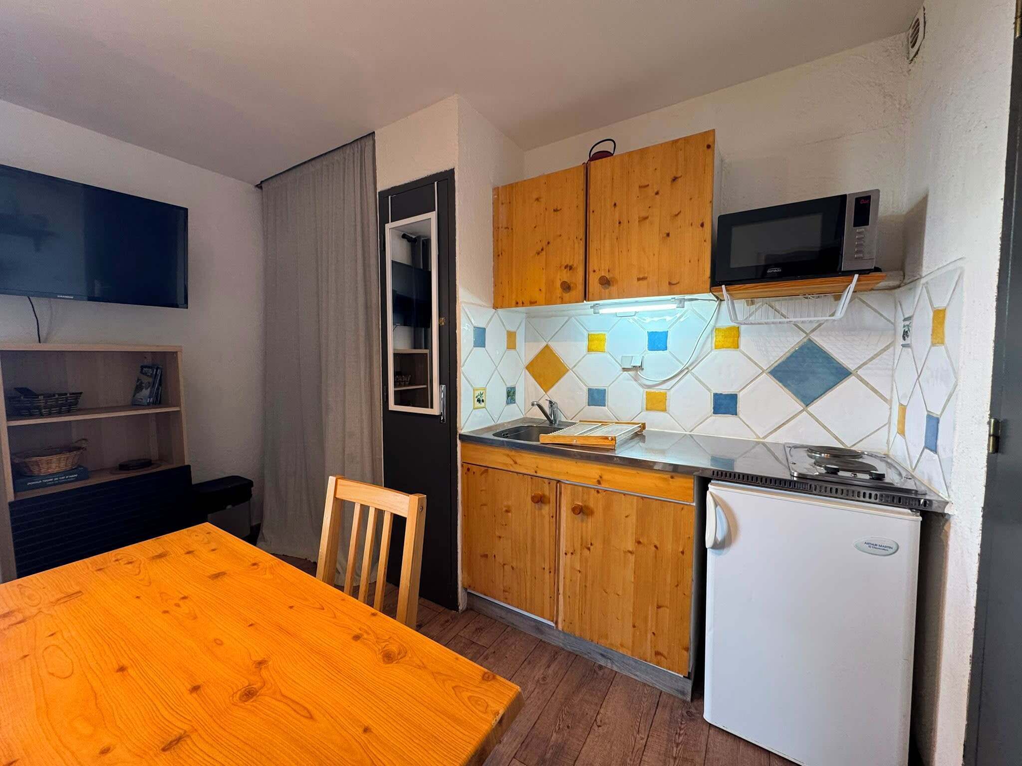 A compact kitchen with wooden cabinets, a microwave, a refrigerator, and a tiled backsplash.