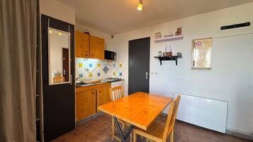 A compact kitchen with wooden cabinets, a dining table, and a microwave.
