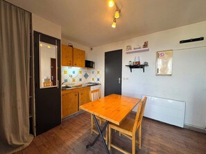 A compact kitchen with wooden cabinets, a dining table, and a microwave. - Studio 16m² - Balcon - Wifi - Risoul Le Villaret (Risoul)