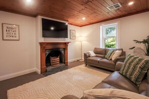 A living room with a fireplace, a sofa, a television, and a window. - Donnybrook Cottages - Donnybrook (Clare)