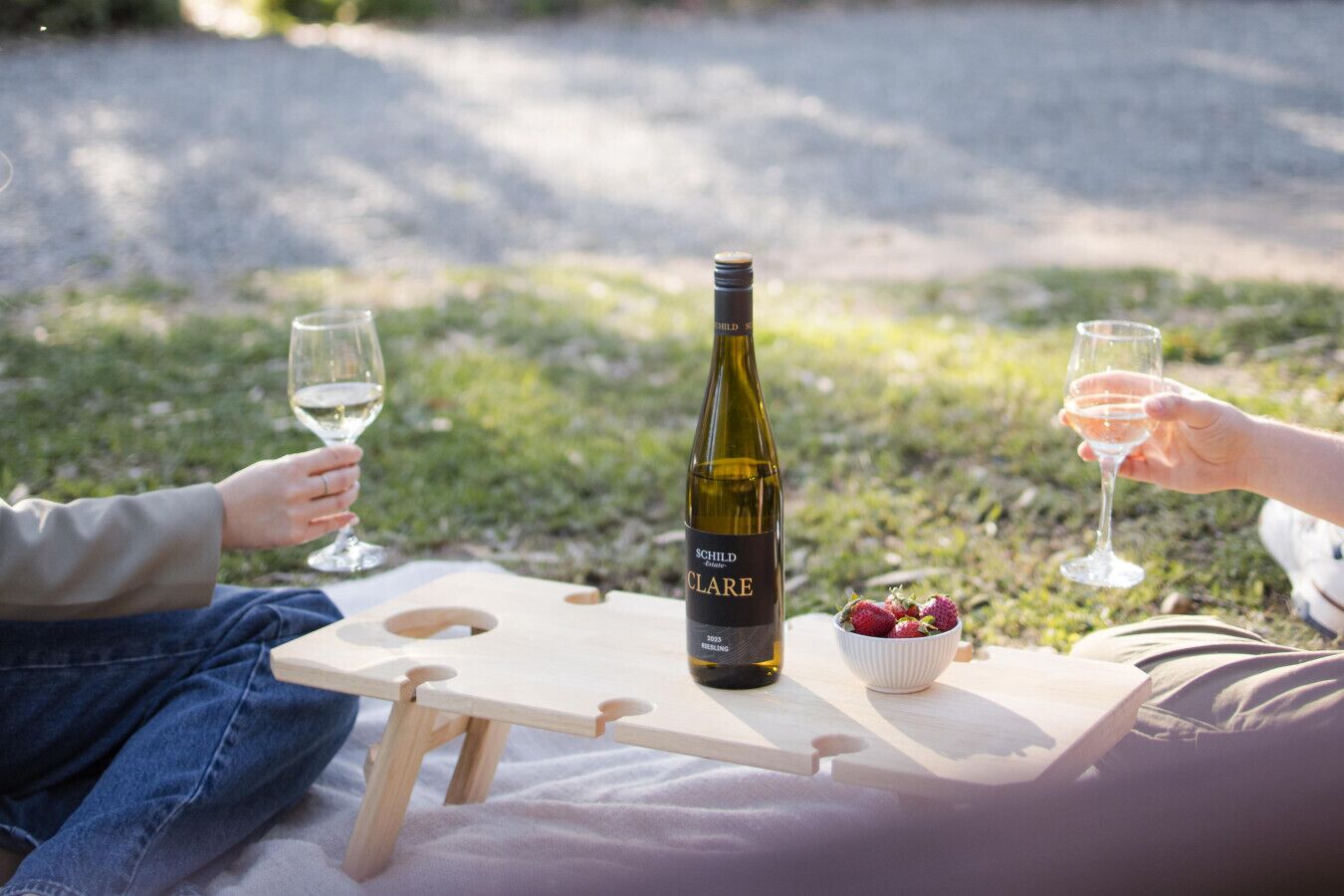 Une table de pique-nique avec une bouteille de vin, des verres et un saladier de fraises, le tout disposé sur une planche en bois.