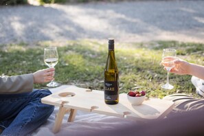 A picnic setup with a bottle of wine, glasses, and a bowl of strawberries on a wooden board.