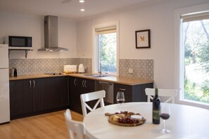 A modern kitchen with dark cabinetry, a microwave, a toaster, and a window with a view of greenery. - Donnybrook Cottages - Donnybrook (Clare)