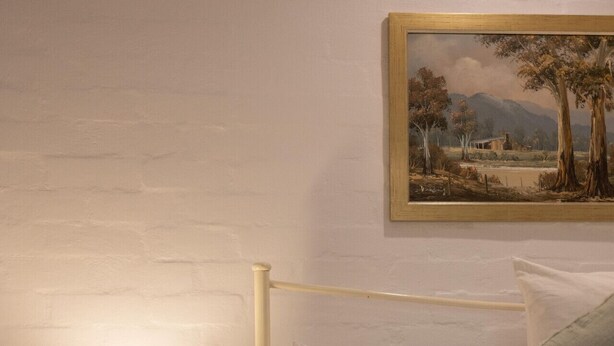Makuuhuone, jossa on sänky, yöpöytä lampun kanssa ja taulu seinällä.