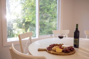 A round table with a bottle of wine, a glass of red wine, a wooden board with cheese, grapes, and crackers. - Donnybrook Cottages - Donnybrook (Clare)