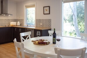 A modern kitchen with a dining table set for two, featuring a bottle of wine and a fruit platter.