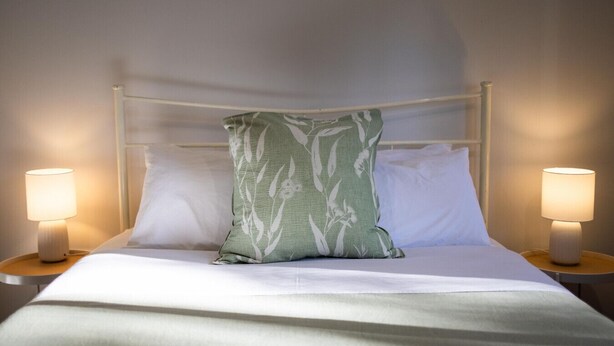 Un lit bien fait, agrémenté d’un seul coussin décoratif, de deux lampes de chevet et d’une tête de lit blanche.