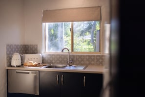 Una cocina con lavavajillas de acero inoxidable, cafetera blanca, tostadora y ventana con vista a follaje.