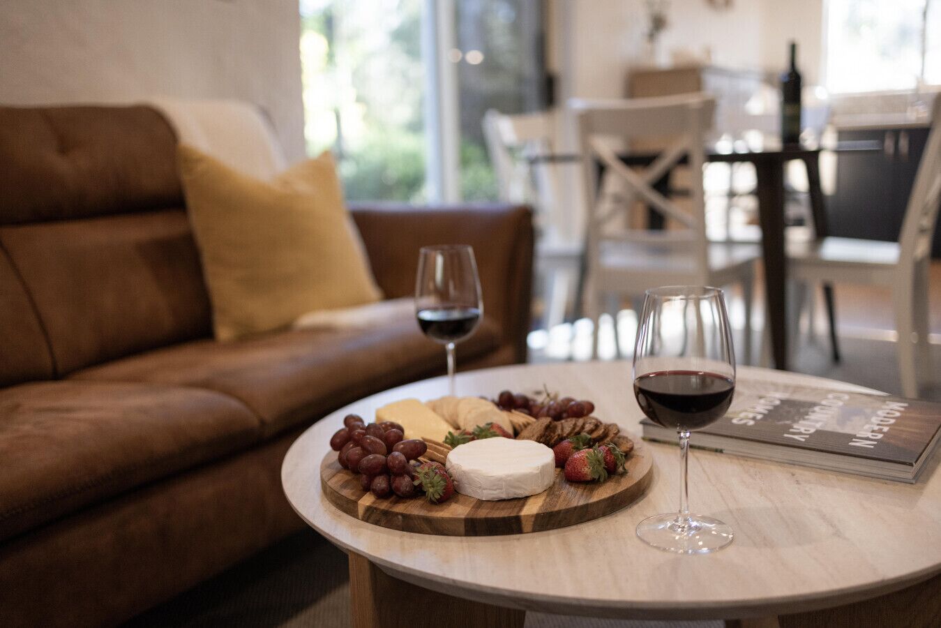 Una mesa de madera redonda con una bandeja de quesos, uvas y copas de vino.