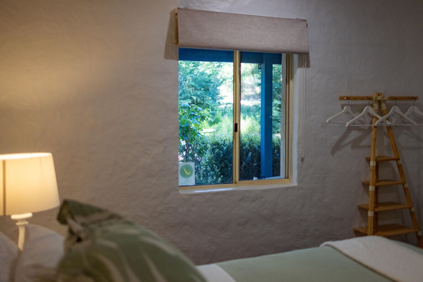 Une pièce avec une fenêtre, un lit, une lampe et une échelle en bois.
