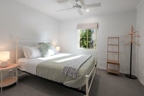 Une chambre à coucher comprenant un lit, des tables de chevet, une fenêtre avec vue, un ventilateur de plafond et un porte-manteau.