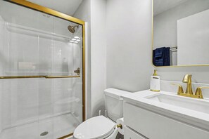 A modern bathroom with a glass shower enclosure, a white toilet, and a vanity with a gold faucet and mirror.