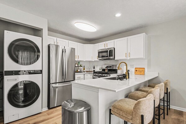 A modern kitchen with stainless steel appliances, a central island, and bar stools.