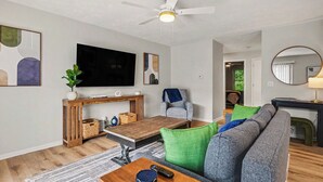 A modern living room with a flat-screen TV, a ceiling fan, a sofa, a coffee table, and a dining area.