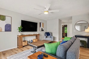 A modern living room with a flat-screen TV, a ceiling fan, a sofa, a coffee table, and a dining area.