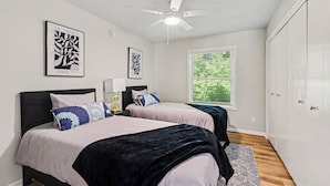 A bedroom with two beds, a ceiling fan, and a window with blinds.