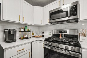 Una cocina moderna con gabinetes blancos, cafetera, copas de vino y estufa.
