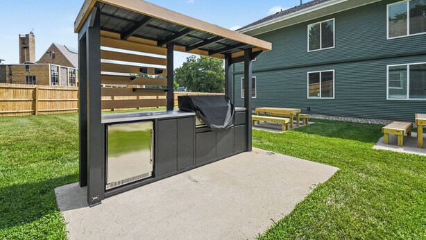 A barbecue area with a metal grill, a wooden bench, and a picnic table.