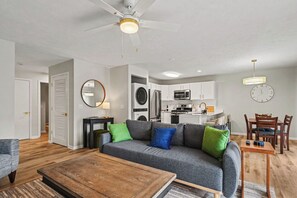 Una sala moderna con un sofá gris, una mesa de centro de madera y un comedor con una mesa y sillas de madera.