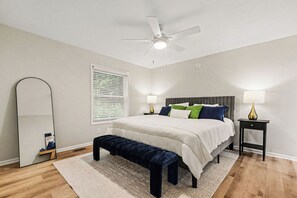 A bedroom with a bed, bedside lamps, a ceiling fan, a bench, and a window with blinds.