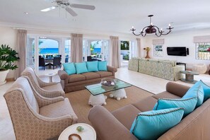 A spacious living room with a sofa set, a glass coffee table, and a view of the outdoor patio. - Stylish Beachfront Villa with Plunge Pool - Still Fathoms (3 bed) (Reeds Bay)