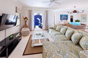 Ein modernes Wohnzimmer mit Flachbildfernseher, einer Couch, einem Couchtisch und Blick auf einen Außenpool.