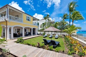 A two-story house with a covered patio, outdoor seating, and a view of the ocean. - Stylish Beachfront Villa with Plunge Pool - Still Fathoms (3 bed) (Reeds Bay)