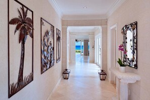 A hallway with artwork on the walls, a stone bench with a potted plant, and a view of the ocean through an open doorway. - Stylish Beachfront Villa with Plunge Pool - Still Fathoms (3 bed) (Reeds Bay)