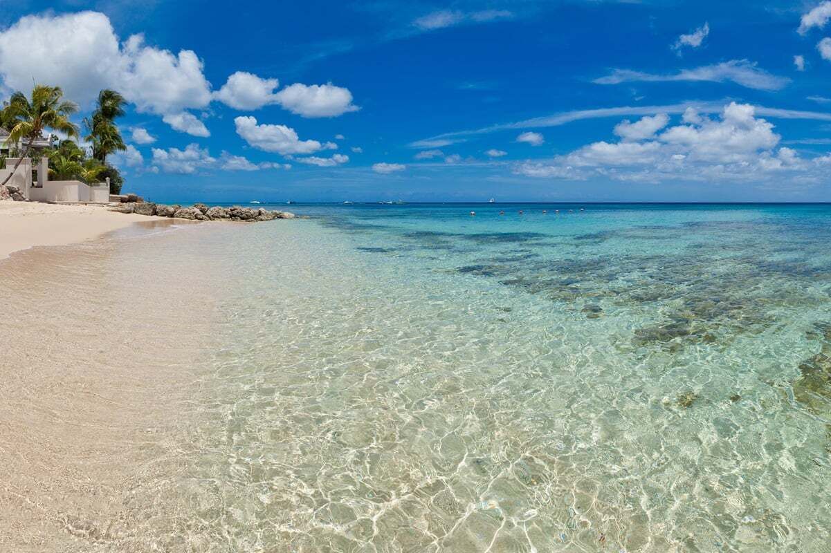 En strand med krystalklart turkis vand, en sandet kystlinje og enkelte palmer.