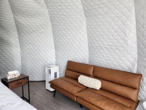 A room with a brown sofa, a small bedside table, and a white air purifier. - Riverside Buffalo Spirit Dome (Calgary)
