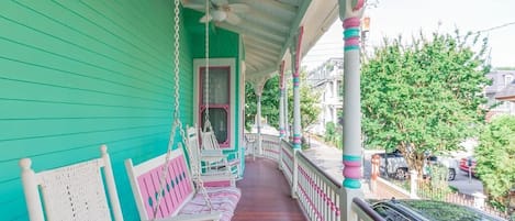 A porch with a swing set, a white bench, and a door leading to an interior space.