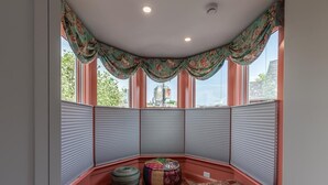 Una stanza d'angolo con una finestra a bovindo, cuscini decorati e vista sull'esterno.