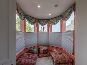 Ein Eckzimmer mit Erkerfenster, gemusterten Kissen und Blick ins Freie.