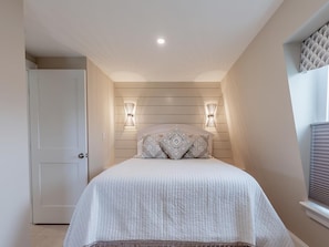 A bedroom with a bed, two wall-mounted lights, a door, and a window with blinds.